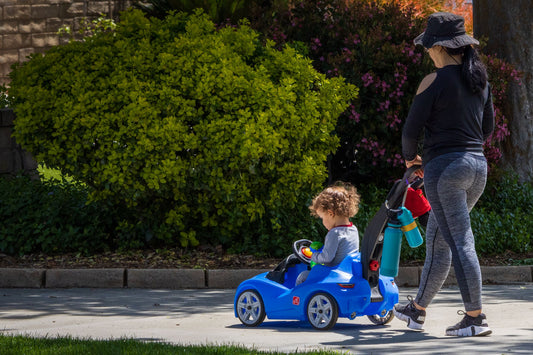 Parent walking alongside a toddler riding a toy car outdoors