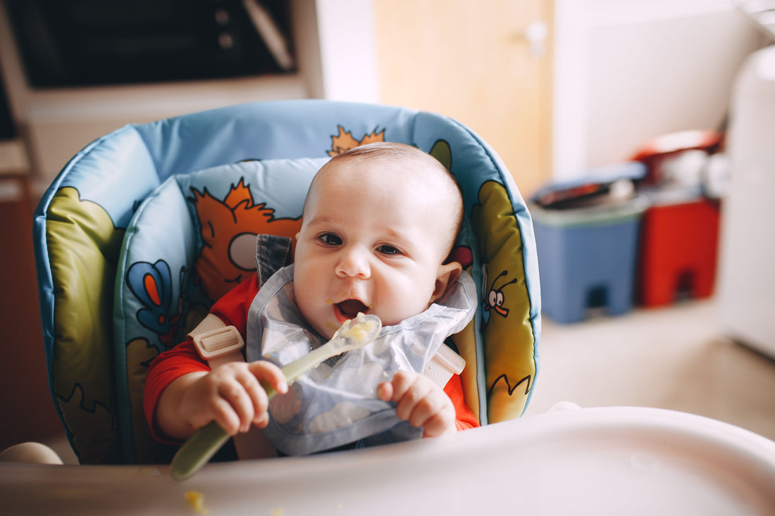 Baby practicing self-feeding with a spoon in a high chair
