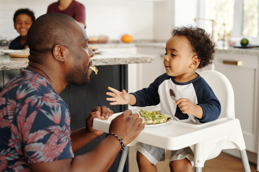Toddler seated in a high chair during a family breakfast with an attentive parent