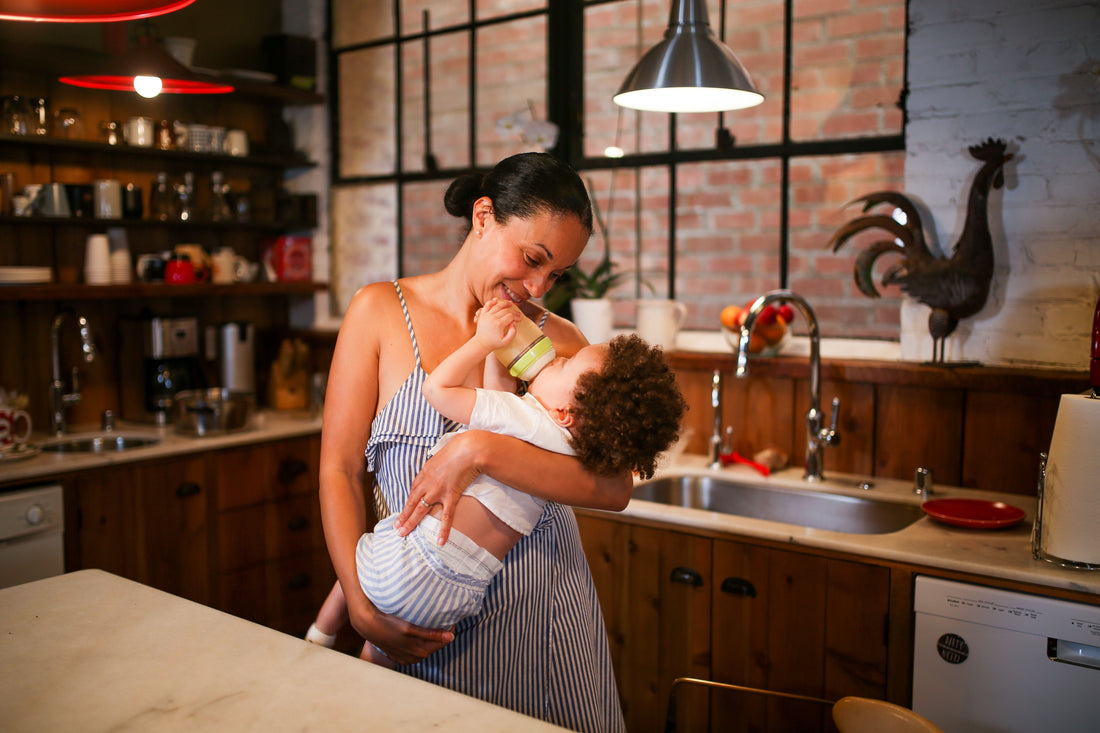 Mother feeding baby a bottle in a warm softly lit kitchen