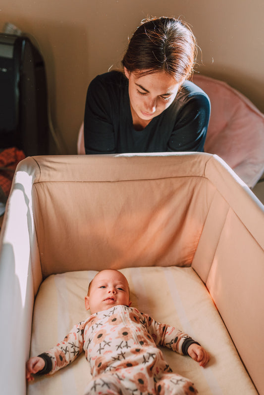 Parent checking on a baby sleeping on their back in a bare bedside sleeper