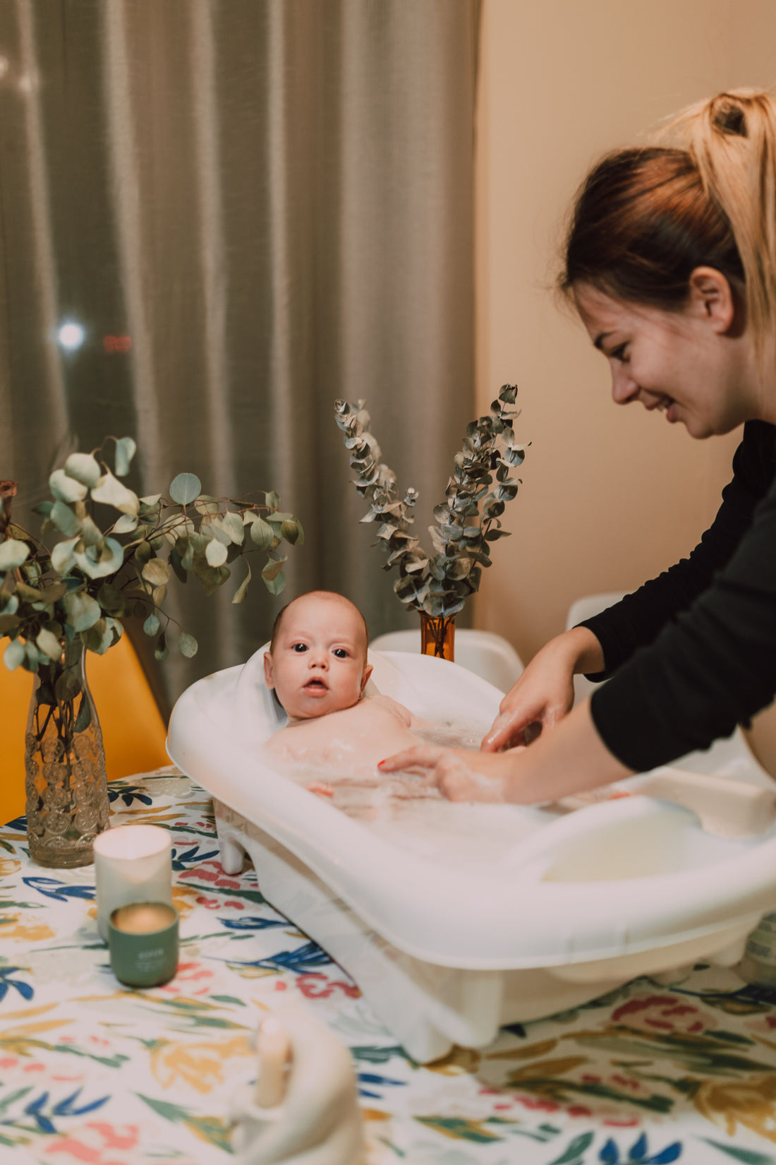 Parent kneeling beside a baby bathtub during a calm bath at home