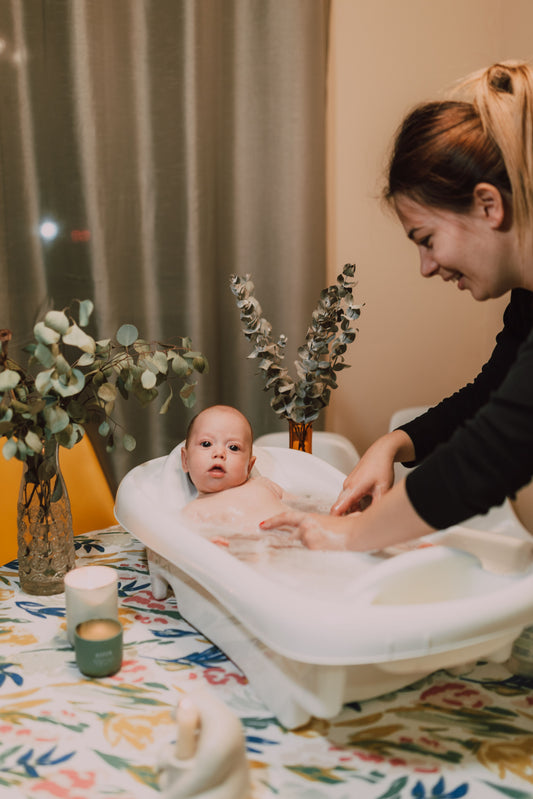Parent kneeling beside a baby bathtub during a calm bath at home