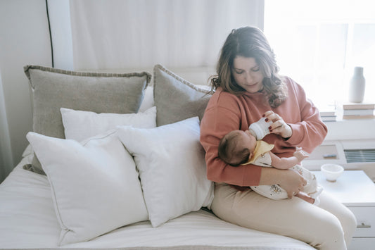 Mother bottle-feeding baby while seated upright with supportive pillows