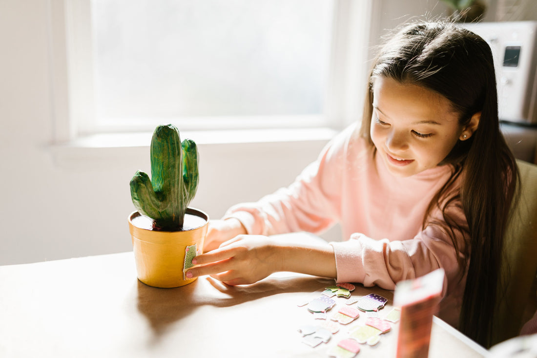Child placing colorful stickers on a potted plant at a bright table